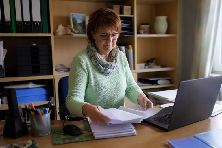 Kassiererin sortiert Rechnungsunterlagen neben einem geöffneten Laptop
